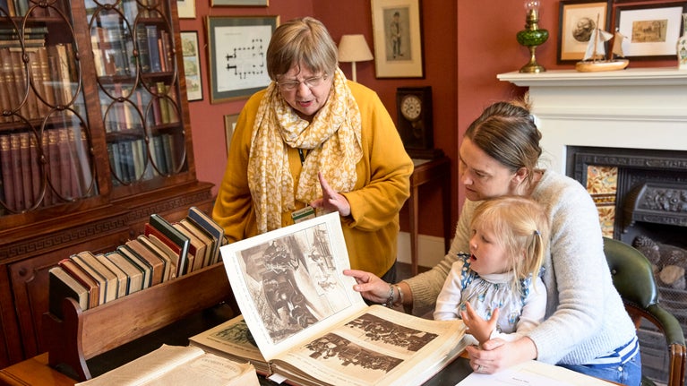 A mother and child read a book with a volunteer at Max Gate, Dorset